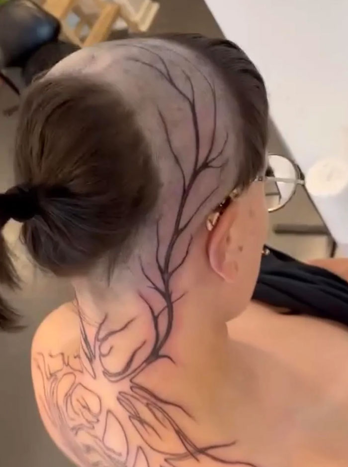 A unique hairstyle featuring a tree branch design shaved into the side of a person's head, revealing a bold and artistic look.