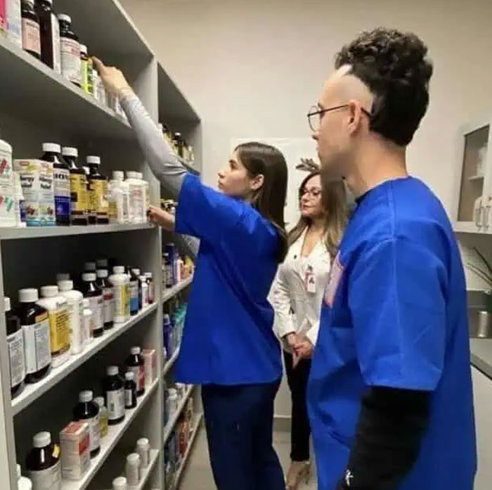 A man with a bold hairstyle, featuring a high fade and curly top, standing in what appears to be a pharmacy aisle.