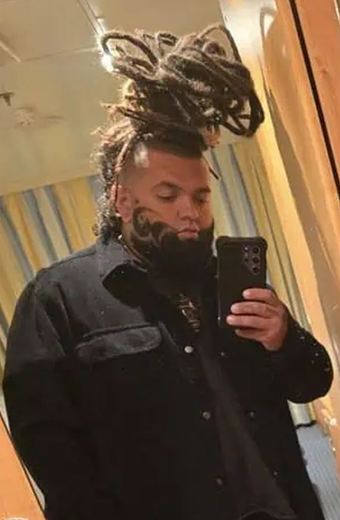 A man with an elaborate mohawk-style dreadlock hairstyle and a sculpted beard, taking a mirror selfie.