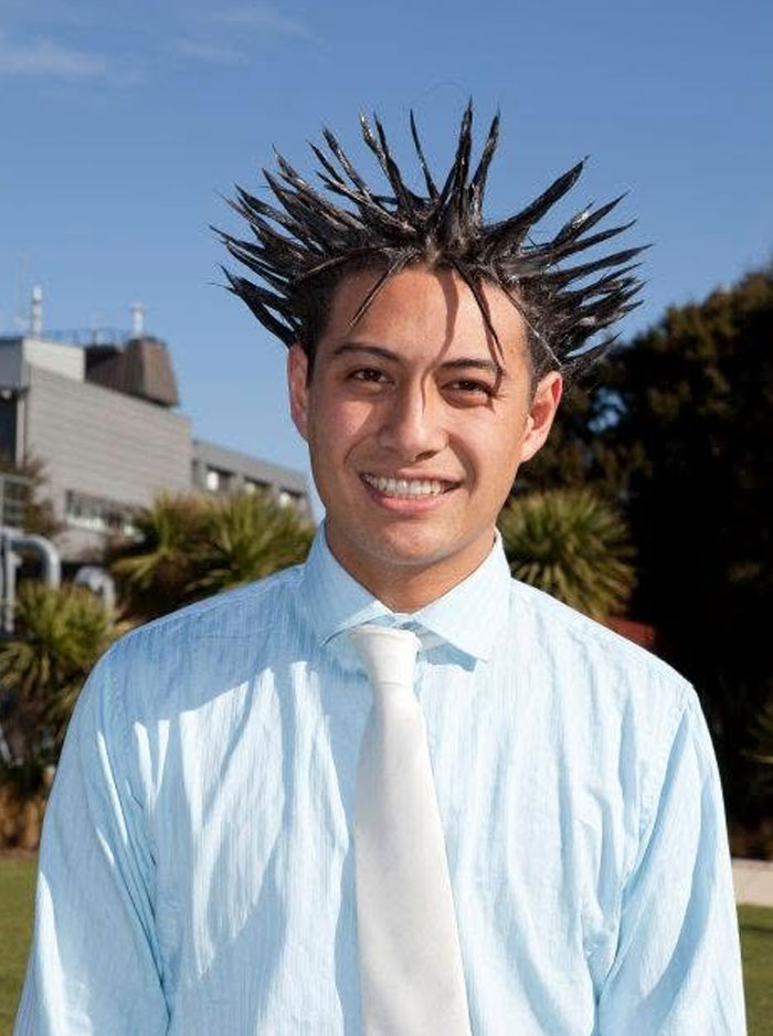 A smiling man in a shirt and tie with his black hair styled into tall, sharp spikes, a truly bold hairstyle.