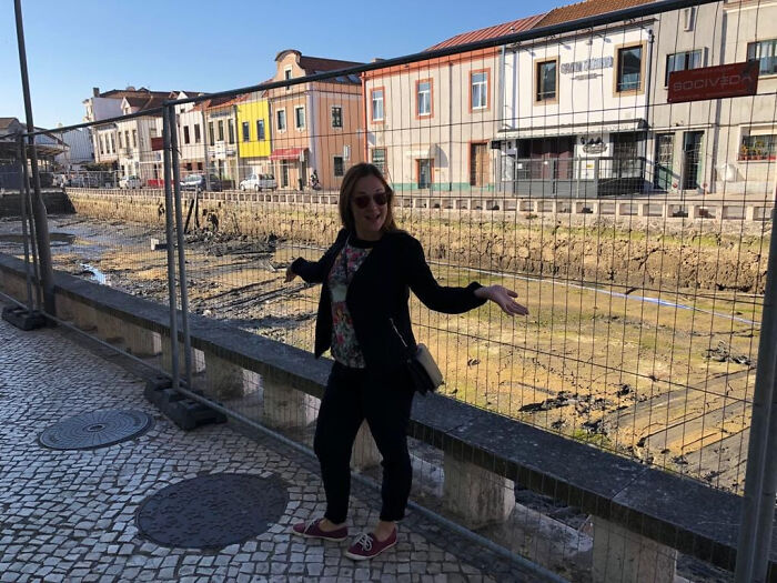 A woman poses in front of a dry, muddy riverbed, an unexpected sight on her trips that didn't go as planned.