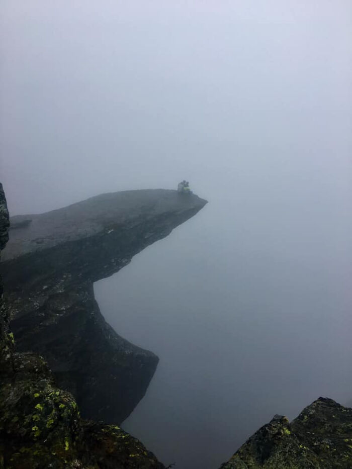 A person stands on a cliff edge obscured by heavy fog, illustrating trips that didn't go as planned.