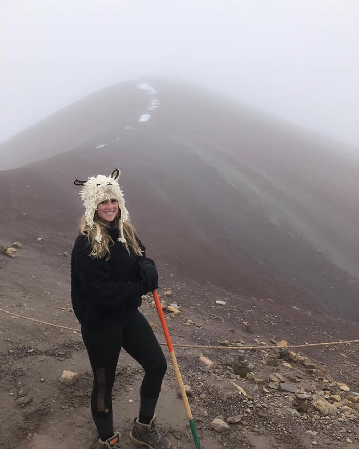 A woman wearing a sheep hat and holding a hiking pole on a foggy mountain path, illustrating a trip experience.