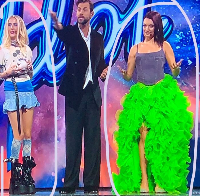 Two women on stage wearing hilariously bad fashion crimes, a light blue skirt with high boots and a bright green ruffled skirt.