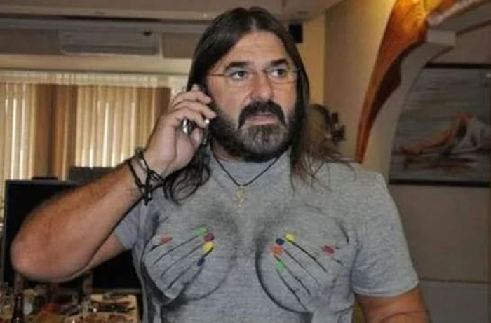 A man with long hair and a beard wearing a grey t-shirt with a humorous breast and nail polish design, a funny fashion crime.