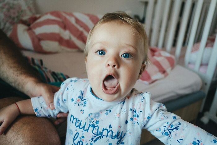 A baby with blue eyes and an open mouth looks surprised at the camera. This baby is an interesting neighbor.