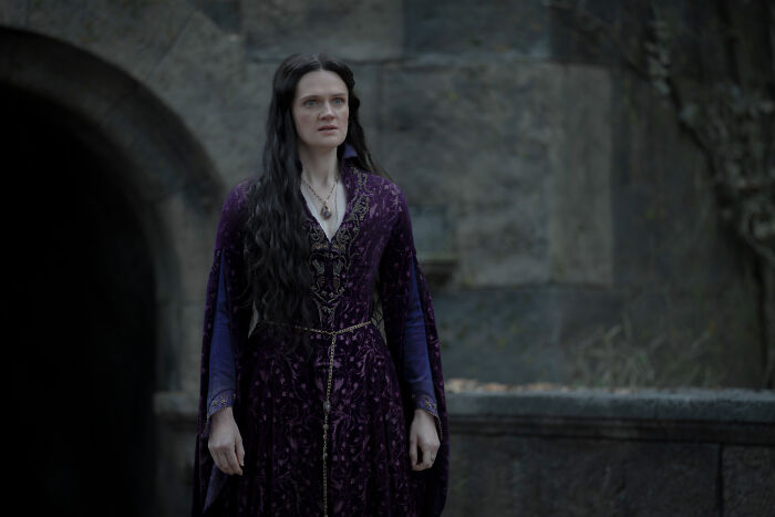 A woman with long dark hair in a purple dress, staring intently in a scene from House of the Dragon. A woman with long dark hair in a purple dress, staring intently in a scene from House of the Dragon.