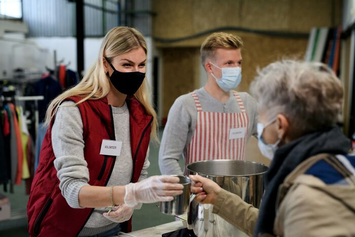 Volunteers in masks serving food to an elderly person, an incredible accomplishment of community support and kindness.