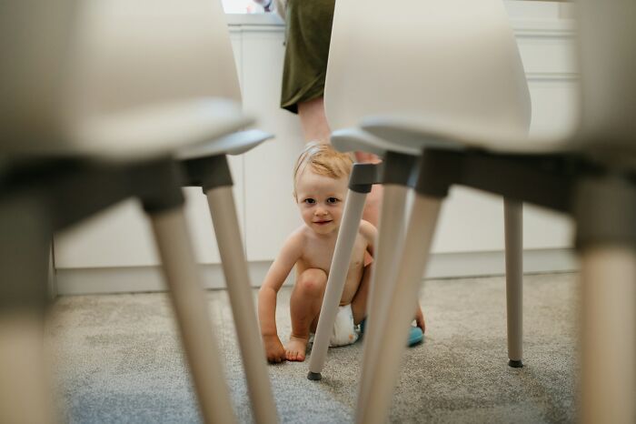 A toddler peeking out from under chairs, looking directly at the camera, highlighting a horrible parent perspective.