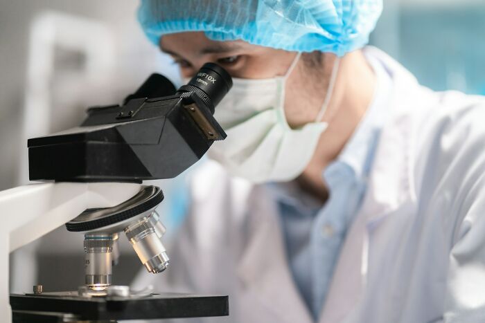 A doctor wearing a mask and lab coat looks into a microscope, symbolizing medical diagnoses and research.
