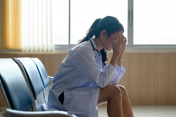 A doctor sits alone, appearing distressed and holding her head, reflecting the hardest diagnoses.