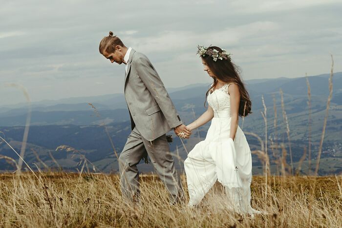 A bride and groom walking hand-in-hand through a grassy field with mountains in the background, a serene wedding moment.