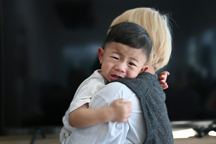 A young boy with short dark hair crying and clinging to a person, visibly scared by a true story.