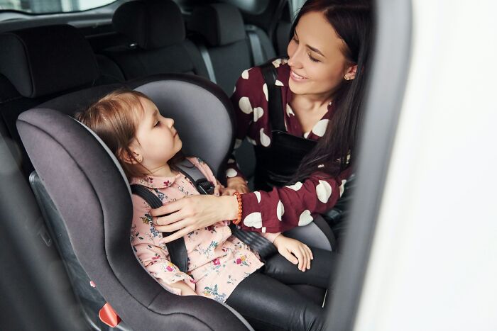 A mother fastening her child into a car seat, focusing on actions that don't scream horrible parent.