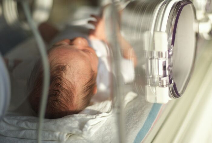 A close-up of a newborn baby with a full head of hair sleeping peacefully in an incubator, representing a crucial aspect of the medical field.