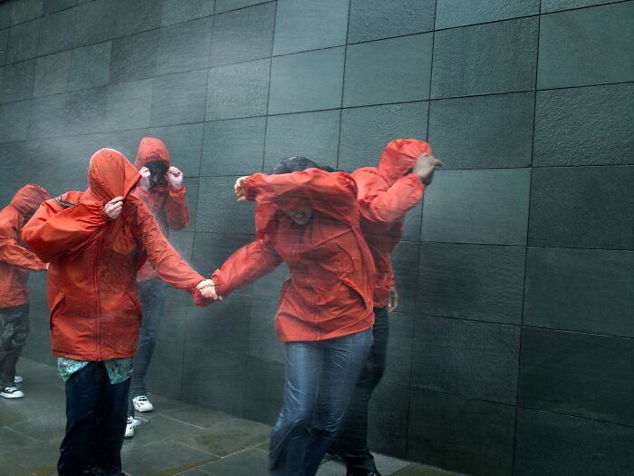 People in red raincoats huddle against strong wind and water, an example of scientific facts in action.