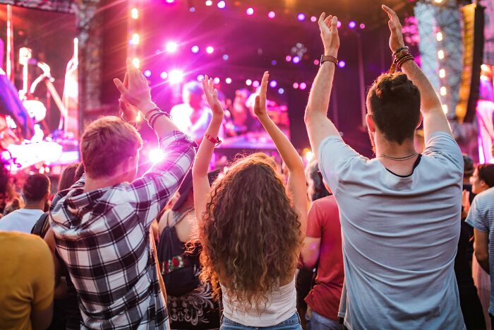 A crowd of people enjoying a vibrant outdoor concert, hands raised in the air, illustrating poverty habits.