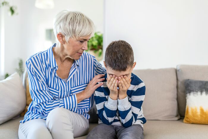 An older woman comforting a crying boy with his face in his hands, illustrating challenging MILs.