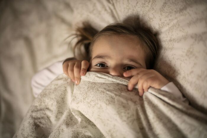 A child peeks from under blankets, representing sad and horrifying diagnoses.