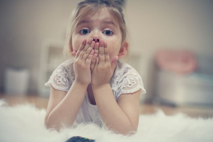 A young girl with wide eyes, hands over her mouth, reacting to scary true stories that question reality.