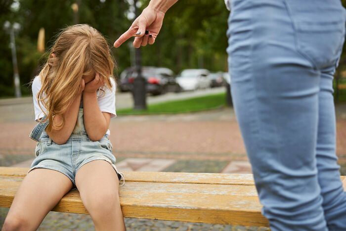 A small child crying and covering her face while an adult points an accusing finger, showing a horrible parent act.