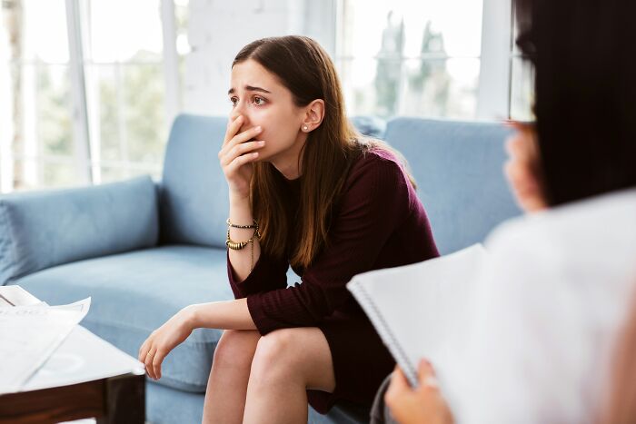 A young woman in distress covers her mouth while talking to a therapist during a therapy session.