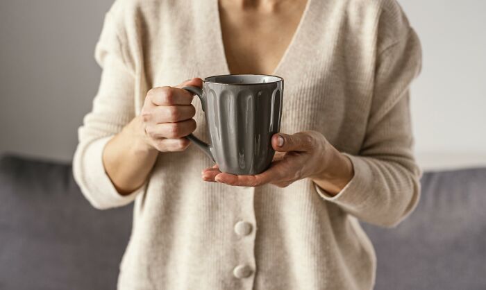 A person holding a grey mug with both hands, representing unhinged house rules for daily routines at home.