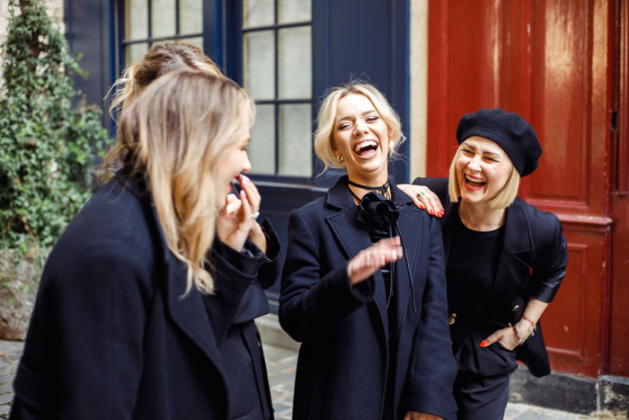 Three women dressed in black coats laughing together outside, fulfilling a man's final wish to make everyone laugh at his funeral. Three women dressed in black coats laughing together outside, fulfilling a man's final wish to make everyone laugh at his funeral.
