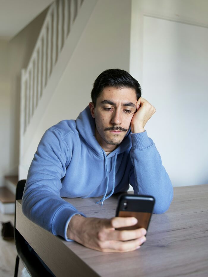 A man looks at his phone with a sad expression, perhaps from receiving sick burns that earned mad respect.