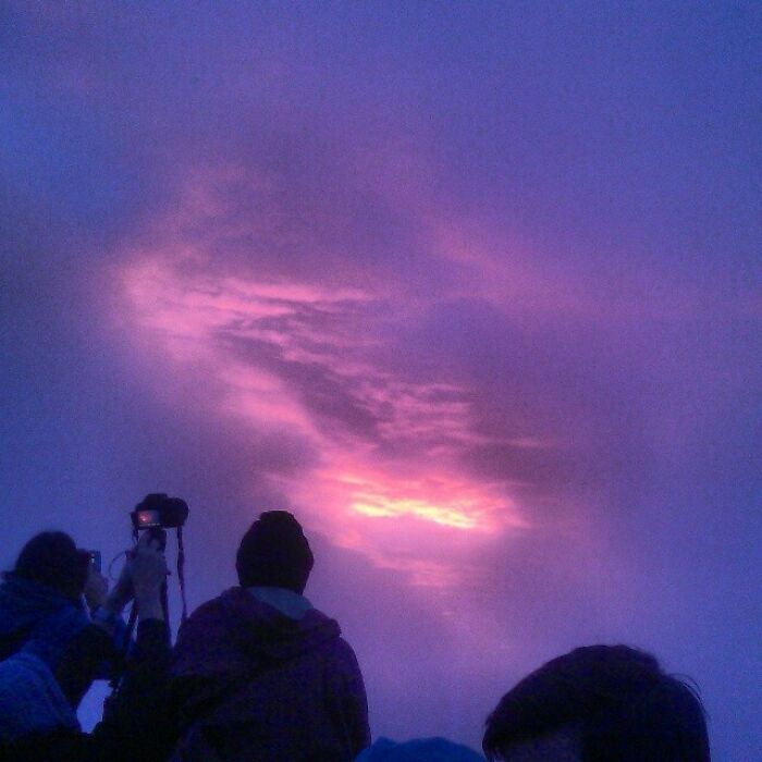 People observe a vibrant pink and purple sky through dense clouds, indicating a trip with unexpected weather.