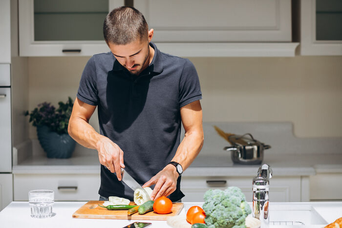 A man chopping vegetables in a clean kitchen, depicting a house rule about cooking and shared spaces.