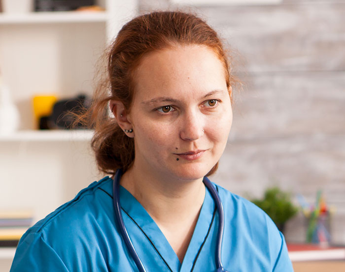A thoughtful female nurse in a blue scrub top, keeping harmless secrets that might warm your heart.