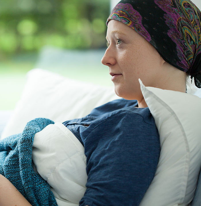 A woman with a headscarf rests in bed, looking away thoughtfully, perhaps holding a personal, heartwarming secret.
