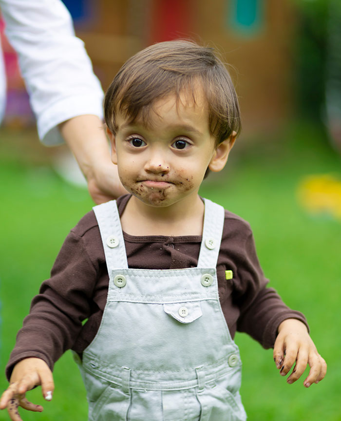 A young child with a messy face and hands, wearing overalls, looking up, embodying the harmless secrets that warm your heart.