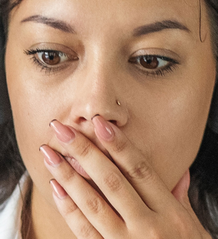 A young woman covering her mouth with her hand, revealing harmless secrets that might warm your heart.