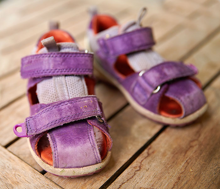 A pair of small, worn purple sandals on a wooden surface, hinting at the simple, harmless secrets of childhood.