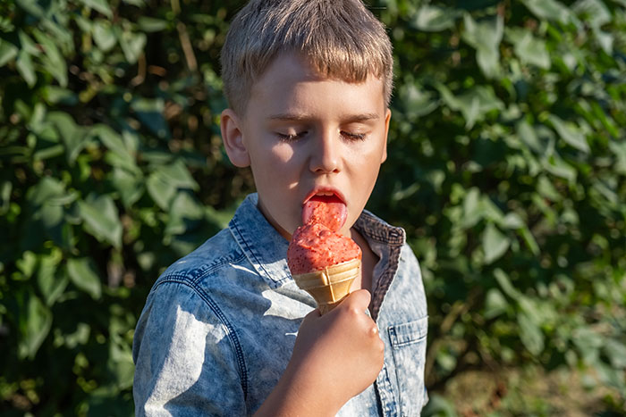 A young boy enjoying a strawberry ice cream cone on a sunny day, representing a harmless secret that warms hearts.