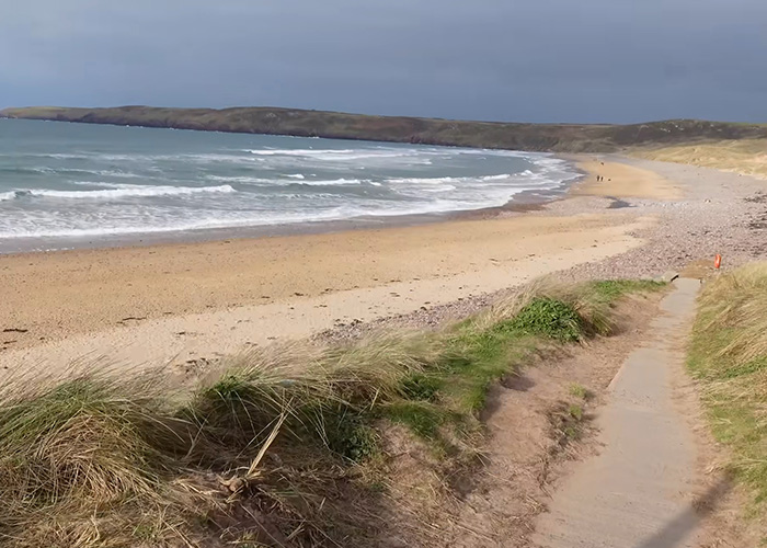 A wide shot of the sandy beach where Harry Potter fans gather, showing the waves and coastal landscape where an undersea cable was rerouted.