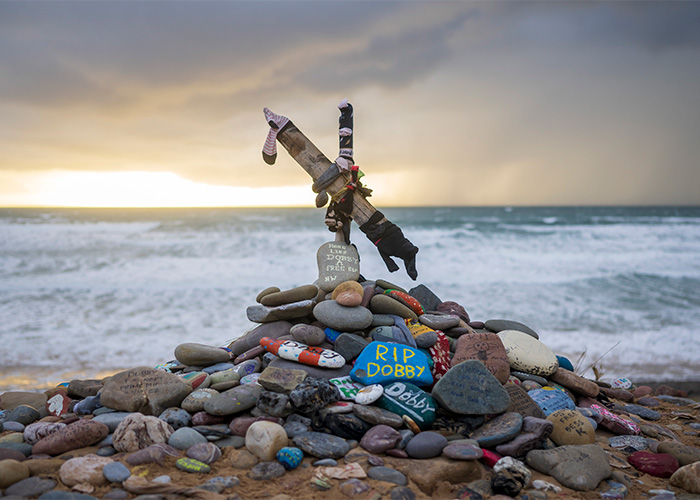 A memorial for Dobby on a beach, covered with painted stones and socks, highlighting how Harry Potter fans reroute undersea cable to protect his grave.