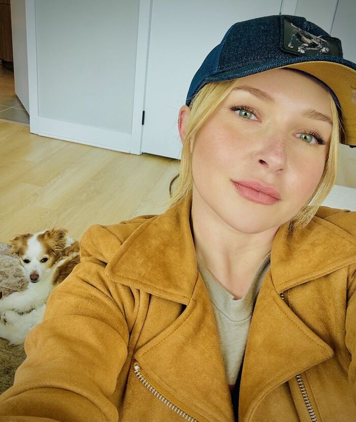 Hayden Panettiere in a yellow jacket and baseball cap, smiling with a dog beside her.