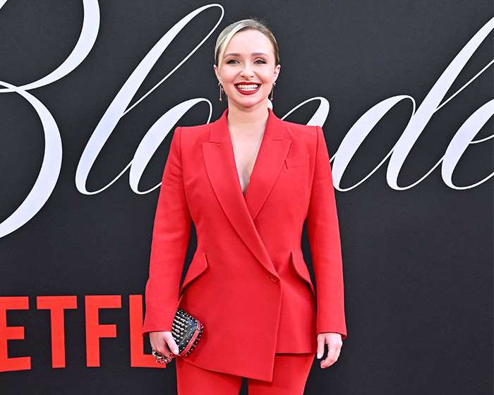 Hayden Panettiere in a bright red suit on a red carpet with a black background. Hayden Panettiere in a bright red suit on a red carpet with a black background.