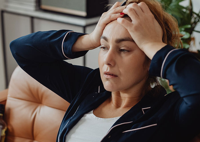 A distressed woman with red hair holds her head in her hands, reflecting on her normal symptoms that surprised a doctor.