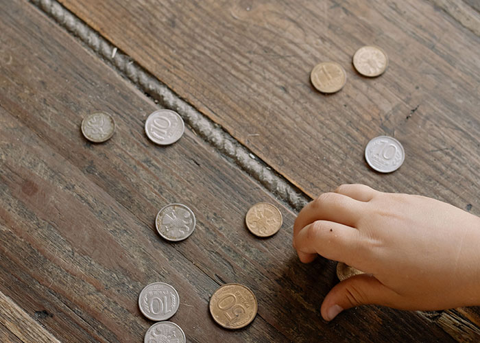 A child's hand reaches for scattered coins on a rustic wooden floor, not related to medical symptoms.