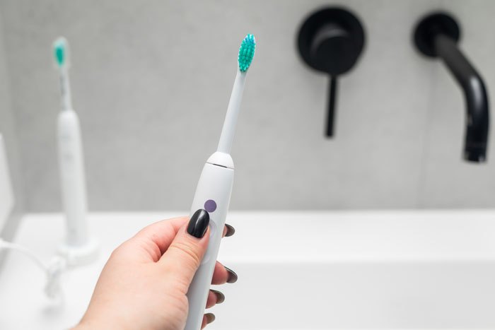 A hand holding an electric toothbrush with a teal brush head over a sink, a sign from the universe.