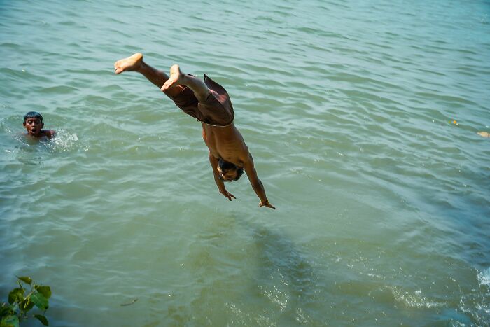 A man diving headfirst into water while another boy swims nearby. Harmless-looking things can be dangerous.