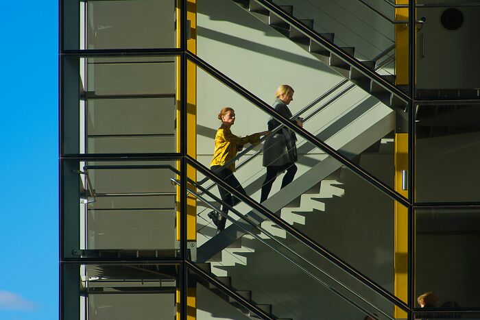 Two women ascending a modern glass staircase, one helping the other. Harmless-looking things can be more dangerous.