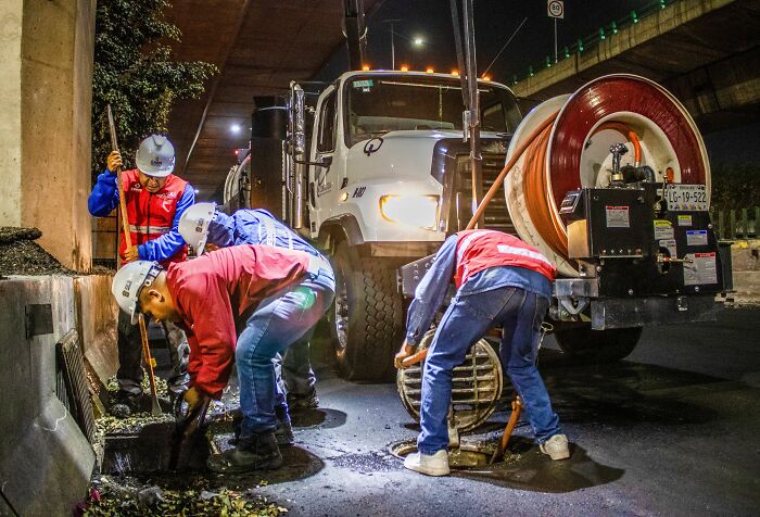 Workers in hard hats cleaning a drain on a street at night, showing harmless-looking things that can be way more dangerous.