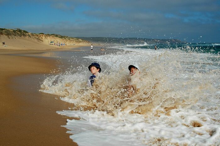 Two children play in crashing waves on a beach; harmless-looking things that can be dangerous.