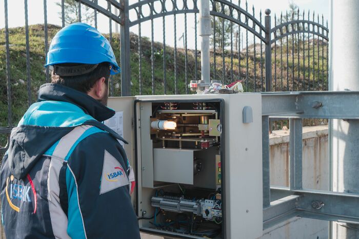 A worker in a hard hat examining dangerous electrical wiring in an outdoor control panel.