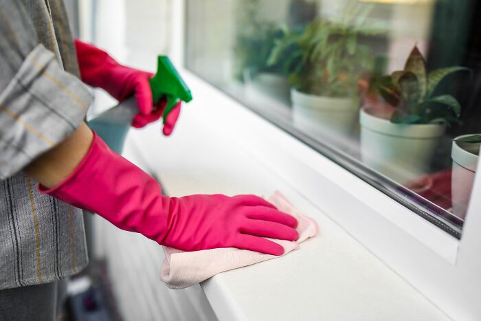 A person in pink gloves cleaning a window sill with a spray bottle and cloth. Harmless-looking things can be more dangerous.